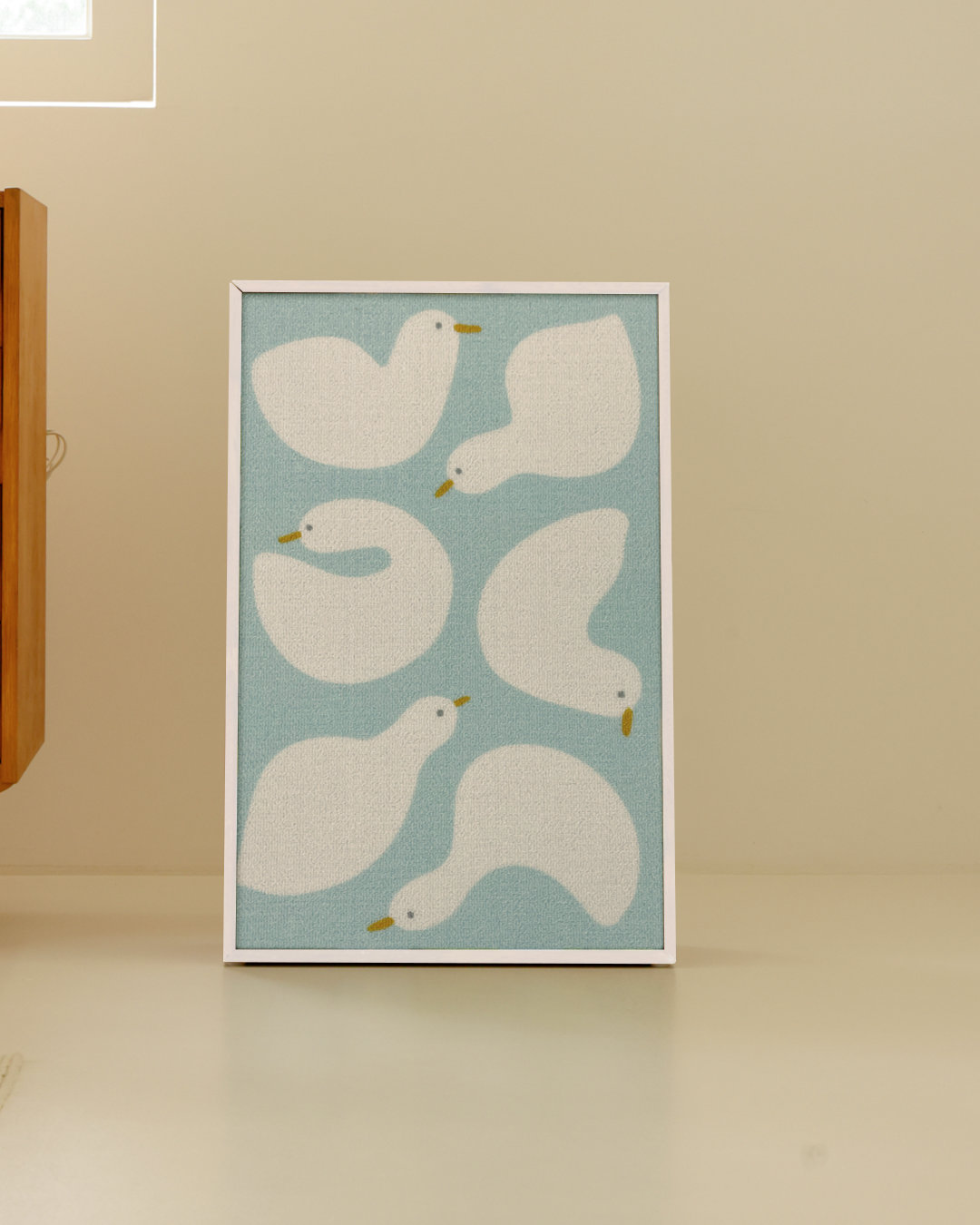 White frame Duck Buddies scratcher propped against a warm beige wall