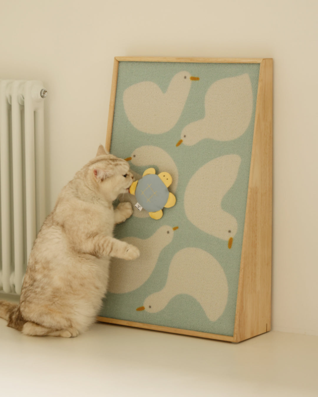Cat scratching the Duck Buddies Art Poster leaning against a wall beside a radiator