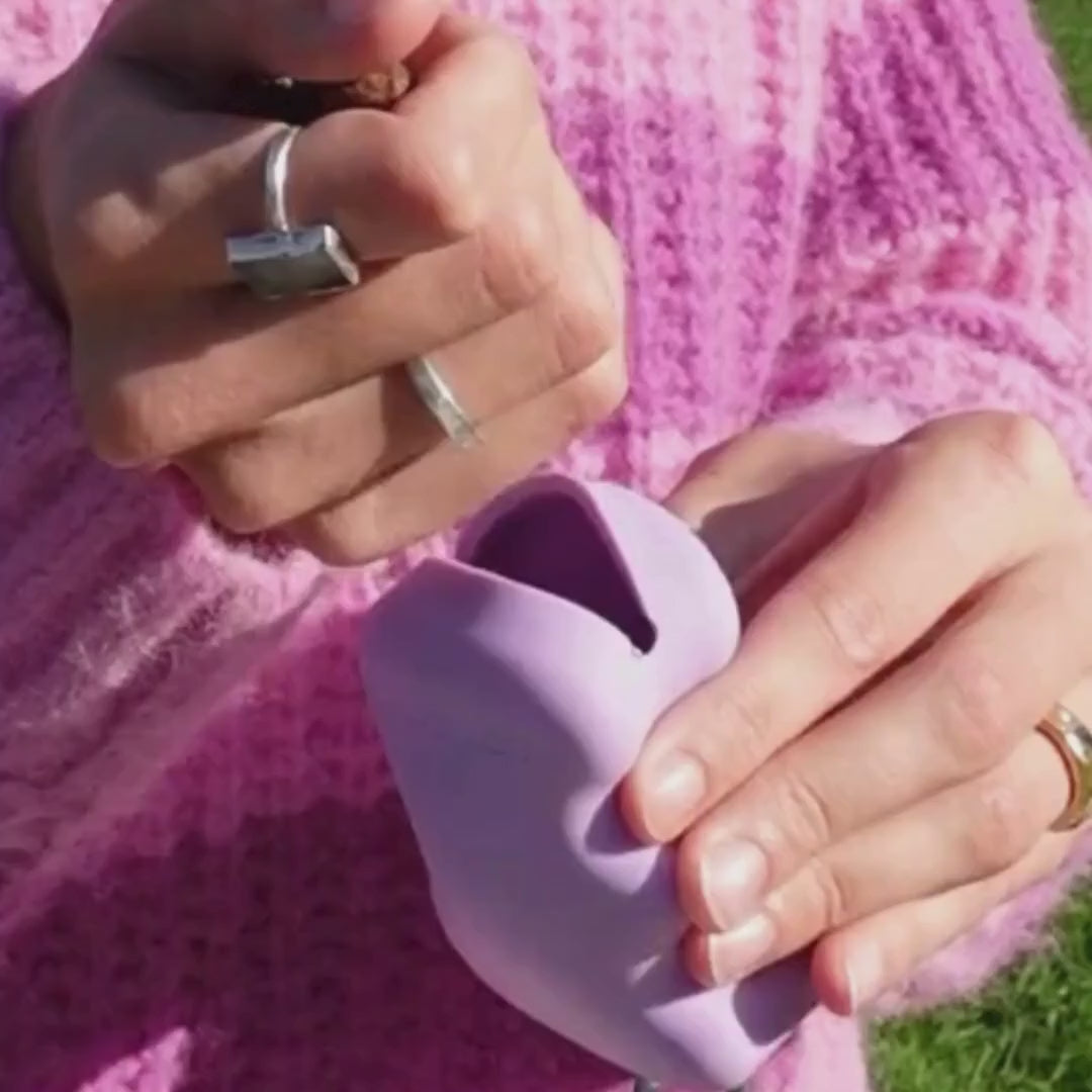 Close-up of a lilac silicone dog treat dispenser being squeezed for quick, one-hand training rewards; portable clip-on treat holder for walks.