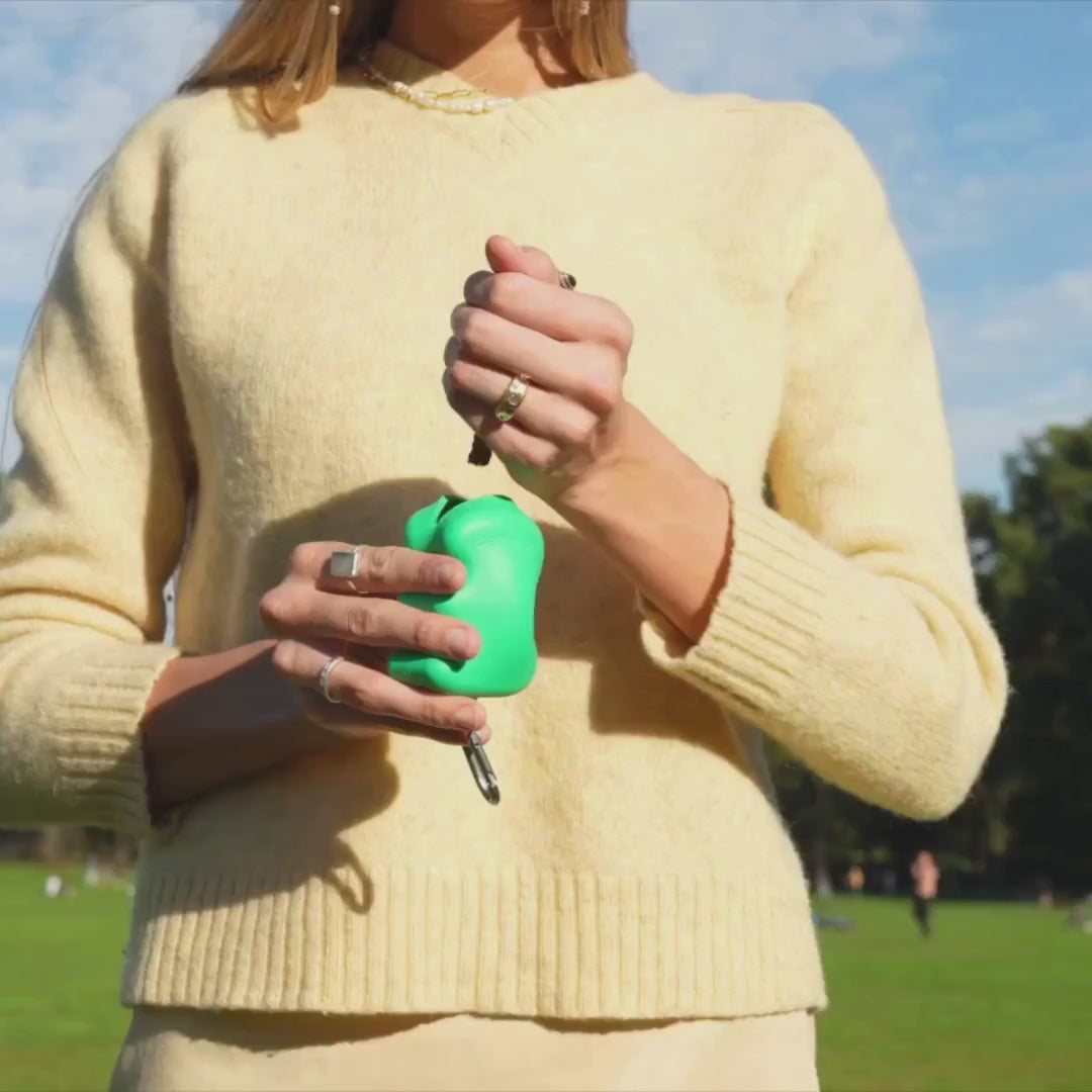 Hand holding a green silicone dog treat dispenser with carabiner, portable squeeze treat holder for training sessions and everyday rewards.