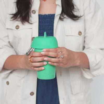 Person holding a green travel dog water bottle with built-in bowl and clip, easy one-hand hydration for daily walks.
